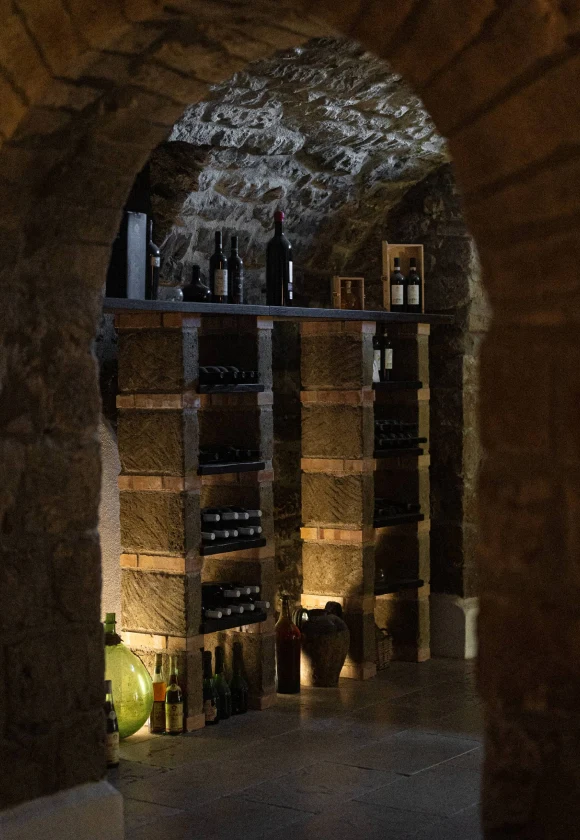 Vista della stanza introduttiva della Cantina del '700 con scaffali in legno pieni di varie bottiglie di vino e contenitori decorativi in vetro.